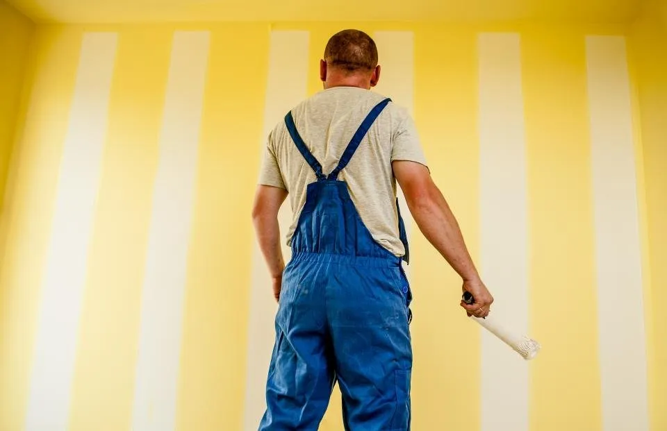 Pintor con rodillo frente a una pared a rayas